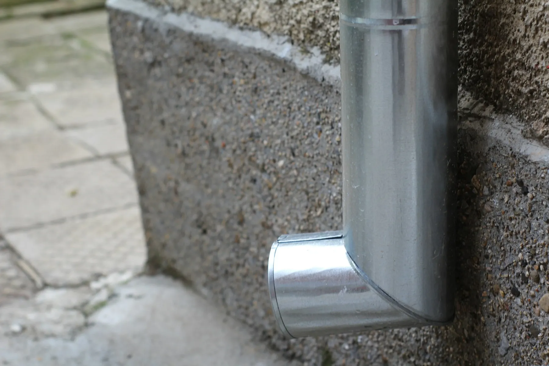 A galvanised steel downpipe and shoe against a pebbledash wall